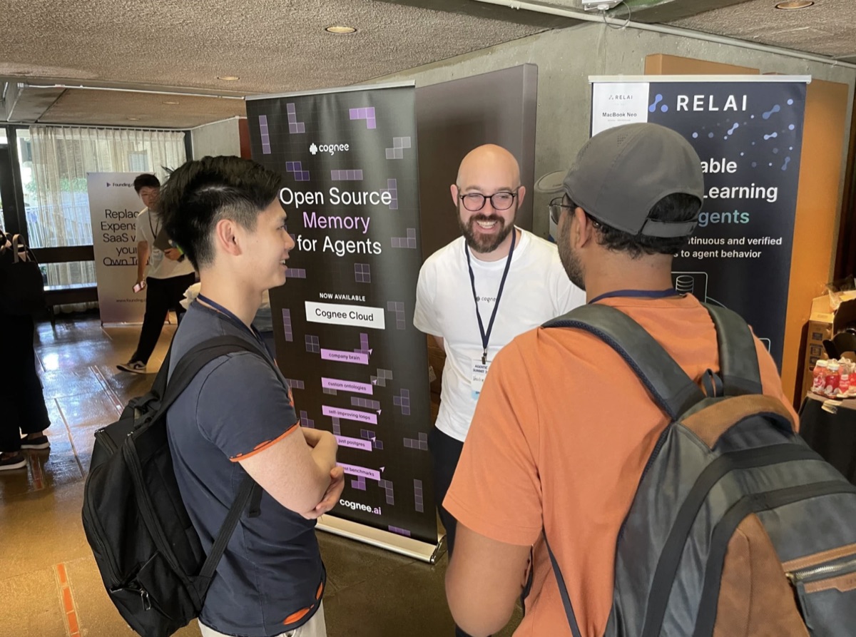 Two attendees talking with a cognee team member in front of the cognee banner at the Agentic AI Summit